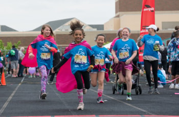 Several girls running across the finish line.  All are wearing blue Girls on the Run t-shirts.