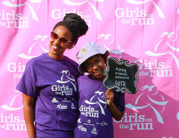 Two people wearing purple t-shirts with the Girls on the Run logo smiling.